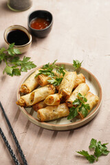 Traditional southeast asian starter dish spring or summer rolls - deep fried dim sum dumplings stuffed with vegetables with soy sauce, fresh coriander on grey plate with black chop sticks, top view