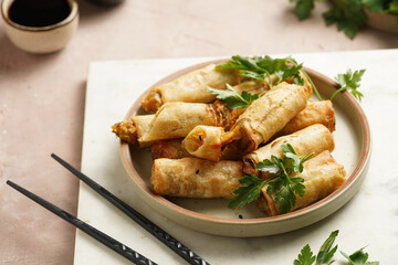 Traditional southeast asian starter dish spring or summer rolls - deep fried dim sum dumplings stuffed with vegetables with soy sauce, fresh coriander on grey plate with black chop sticks