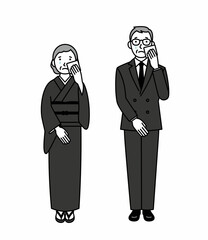 涙を拭く喪服のシニア男女