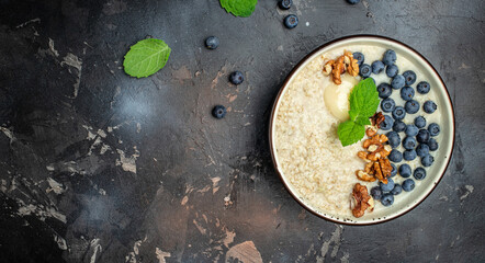 Oatmeal porridge in a bowl with fresh blueberries and nuts on a dark table. Healthy breakfast. Super food healthy eating vegetarian vegan food. Long banner format. top view