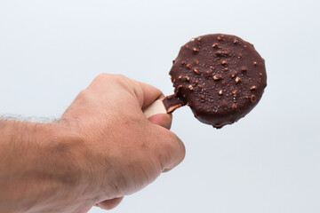 a hand holding an round chocolate ice cream and almond pieces on white background