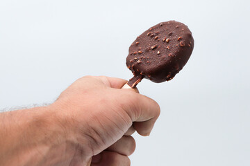 a hand holding an round chocolate ice cream and almond pieces on white background