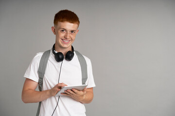 Ginger male student using digital tablet at grey background