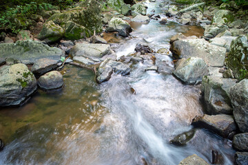 Naklejka na ściany i meble Closeup of long exposure stream flowing around large gray stones