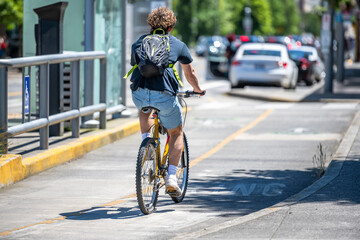 Young man cyclist with a backpack hurries to the place of study while driving along a long bike path along the street of an urban city