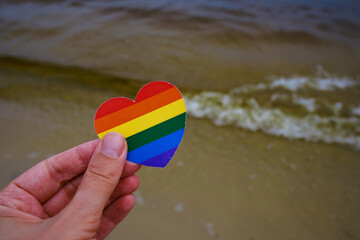 Obraz premium Rainbow heart from paper in woman hands. LGBT flag. LGBTQIA Pride Month in June. Lesbian Gay Bisexual Transgender. Gender equality. Human rights and tolerance. Rainbow flag 