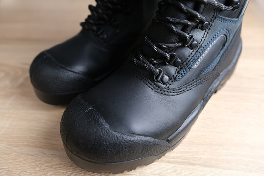 close-up of pair of new black work boots made of leather with reinforced cape, high top on wooden floor, concept of special protective professional shoes, professional work safety