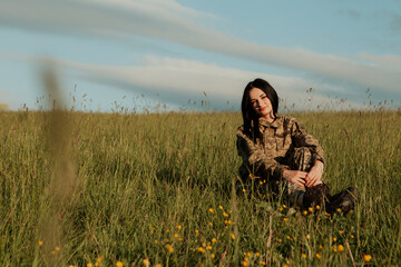 Female soldier sitting on grass in the field dressed in military uniform. Armed Forces of Ukraine. Woman serving in ukrainian army.