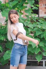 Portrait of a young woman in jeans and a snake by the wild plants in an urban environment