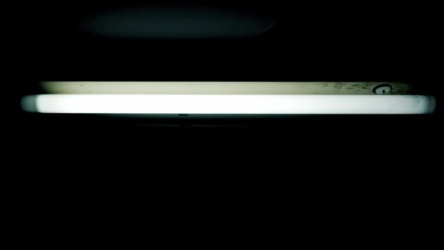 Moving towards (zoom in) a scary, ominous flickering neon light inside a basement. Something dangerous could be hiding in the shadows. Handheld closeup shot.
