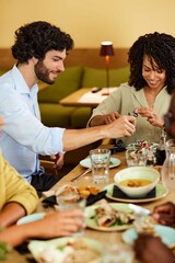 A multiracial group of people sits together in a restaurant and eating dinner.