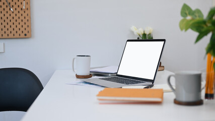 Computer laptop with blank screen, coffee cups, notebook and houseplant on white table