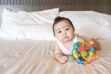 Portrait of cute little asian baby girl wearing white bodysuit lying on white beedsheets and toy at home.