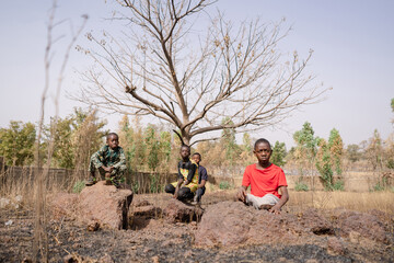 Group of four sad looking African boys sitting on a dried up farm doing nothing; crop failures, job...