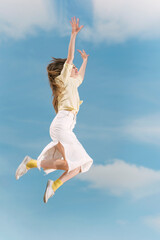 Girl with her hands raised up during jump against the blue sky. Young woman flying high in blue sky.