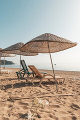 Sunbeds and rattan parasols on sandy seaside.