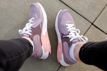 Womens legs in pink sneakers. Womens sports shoes on concrete paving slabs. View from above