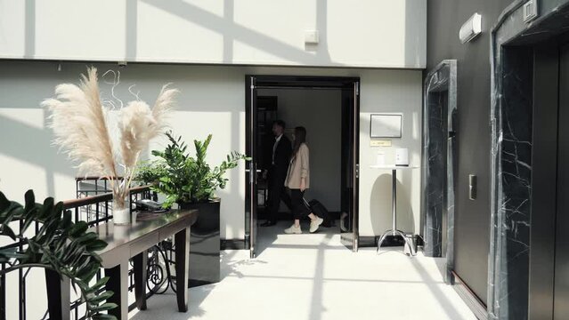 A stylish business couple is checking into a hotel. Businessmen walk along the corridor of the hotel and carry a suitcase. Full length of tourist in the hall. Business, travel and people concept.