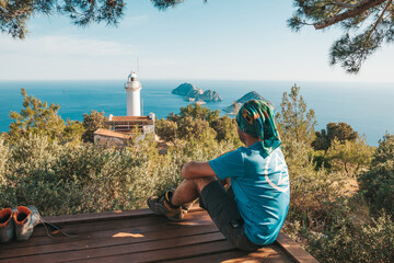 The traveler sits against the backdrop of a picturesque seascape with small islands and an old...