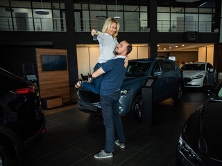 Fototapeta na wymiar Happy caucasian couple hugging while buying a new car in a car dealership.