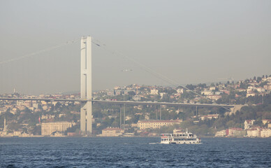 Istanbul, Turkey - April 2022: Stunning view over Bosphorus Bridge and a boat near it from the cruise ship along Bosphorus in the evening. Haze and fog