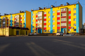 View of colorful multi-colored residential buildings. The buildings are painted yellow, blue and red. Improvement in the settlements of Siberia. Palatka urban-type settlement, Magadan region, Russia.