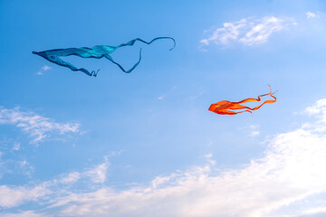 Orange and blue kites on the background of a blue sky with clouds