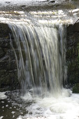 Small waterfall with fresh current at small lake Schwarzweiher in Palatinate landscape, sunny spring day, concept: refreshment, outdoor, power (vertical), Enkenbach-Alsenborn, RLP, Germany