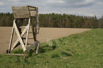 Wooden raised blind with camouflage net at a freshly ploughed field, sunny spring day, concept: hunt (horizontal), Enkenbach-Alsenborn, RLP, Germany