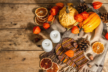 Autumn cozy composition. Scarf, warm mittens, candles, pumpkins, fall decor. Wooden background