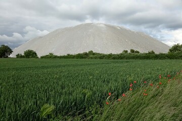 Potash mountain Wetterberg (Kalimandscharo) with green grain field in the foreground under a cloudy spring sky (horizontal), Giesen, Lower Saxony, Germany