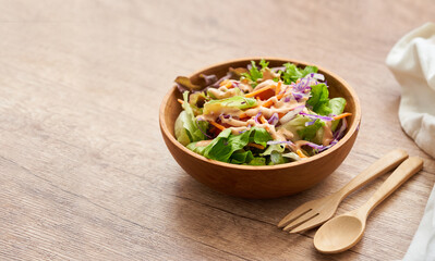 mix salad from green leaves and cherry tomato in a wooden bowl with a spoon and fork on white wood table background. copy space