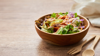 mix salad from green leaves and cherry tomato in a wooden bowl with a spoon and fork on white wood table background. copy space