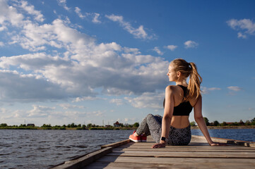 Slim fitness woman sitting and relax after trainings on the pier in sunset