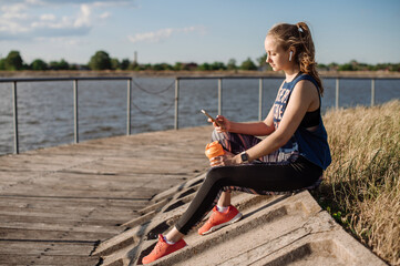 Sporty woman in sportswear chilling on pier at the water background