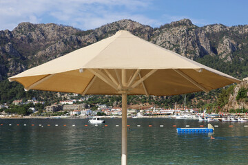 Beach vacation, sun umbrella on sea background. View to mountains on Mediterranean coast, tourist boats and resort town