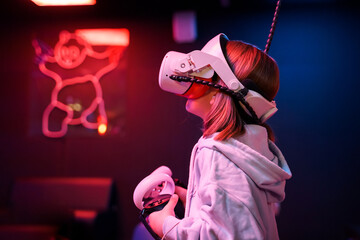 Girl playing vr game in 3d glasses headset. Virtual reality simulation club for gamers.Joysticks for futuristic video shooting game in hands.Innovation technology.Fun entertainment in neon light room