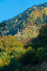 Picturesque autumn landscape, power line support in a mountainous area on a sunny day. High-voltage power transmission lines in the mountains. Vertical photo