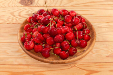 Red sweet cherries on stems on the wooden dish