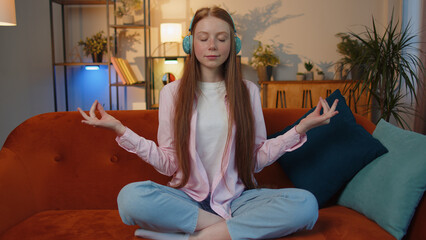Obraz premium Keep calm down, relax, inner balance. Young redhead child girl breathes deeply with mudra gesture eyes closed meditating with concentrated thoughts, peaceful mind sit at home in living room on couch