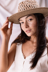 Portrait of beautiful woman in straw hat and white dress posing isolated over textile background. Romantic look