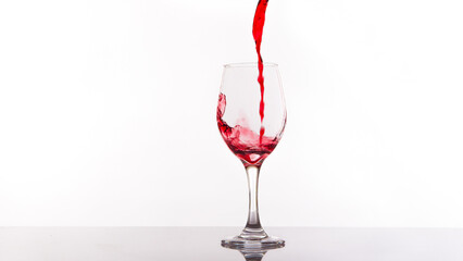 Red wine being poured into wine glass on white background.