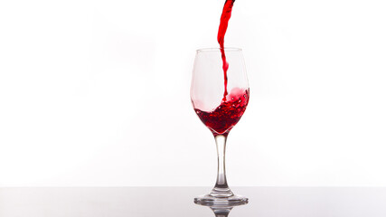 Red wine being poured into wine glass on white background.