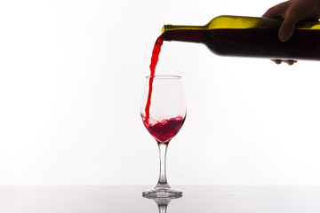 Red wine being poured into wine glass on white background.