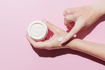 Woman applying cosmetic cream into hands against pink background. Skin care and body treatment. Mockup for designers