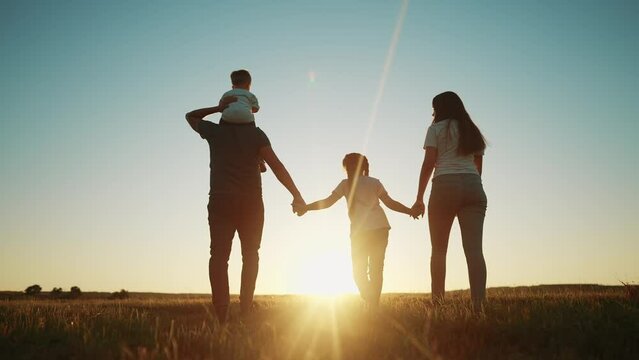 people in the park. happy family walking silhouette at sunset. mom dad and daughters walk holding hands in the park. happy family childhood dream concept. parents and children go sun back silhouette
