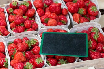 Red strawberries market baskets and black blank copyspace sign. Cups of fresh sweet quality...