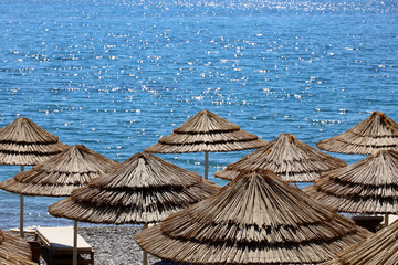 Empty pebble beach with wicker parasols and deck chairs. Picturesque view to sea with shining water, summer resort