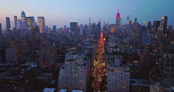 Wide New York road with hundreds of cars moving along. Descending drone footage over the light street at sun down.