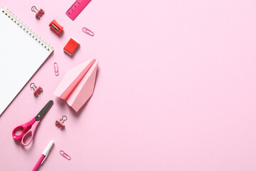 Flat lay school supplies on pink background. Top view table with notepad, scissors, clips, pen, paper airplane. Back to school concept.